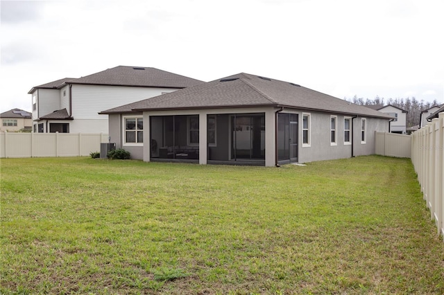 rear view of house featuring roof with shingles, a yard, stucco siding, a sunroom, and a fenced backyard