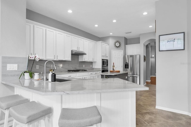 kitchen with arched walkways, a peninsula, stainless steel appliances, under cabinet range hood, and a sink