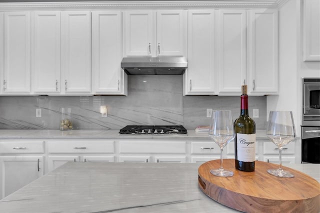 kitchen with white cabinets, under cabinet range hood, stainless steel appliances, and decorative backsplash