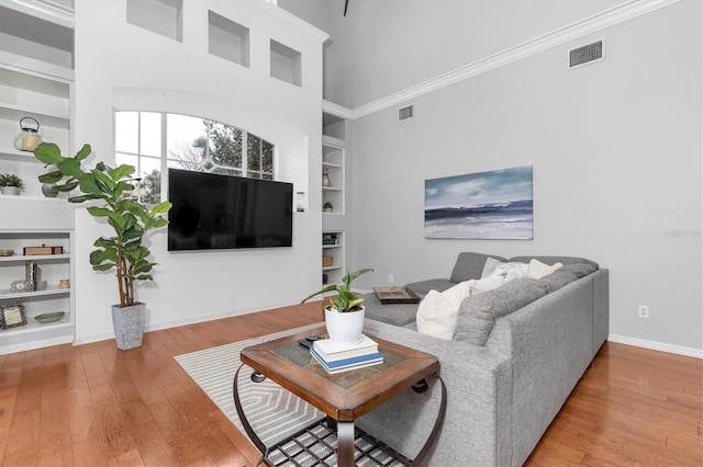 living area with built in features, visible vents, ornamental molding, baseboards, and hardwood / wood-style flooring