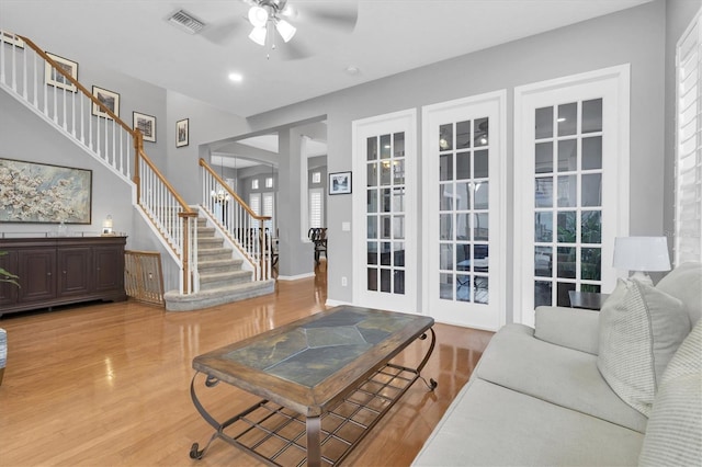 living area with arched walkways, light wood-style flooring, visible vents, a ceiling fan, and stairway