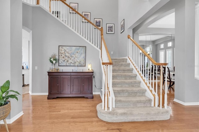 stairway featuring arched walkways, a high ceiling, wood finished floors, and baseboards