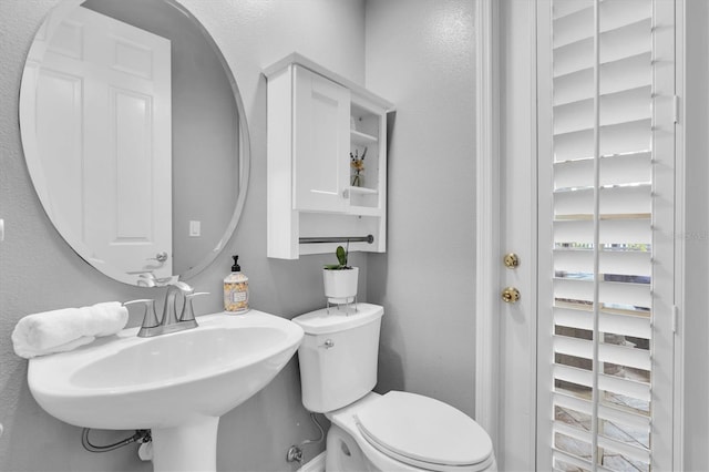 half bathroom featuring toilet, a sink, and a textured wall