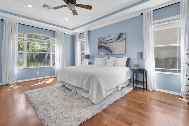 bedroom with visible vents, baseboards, a tray ceiling, wood-type flooring, and crown molding