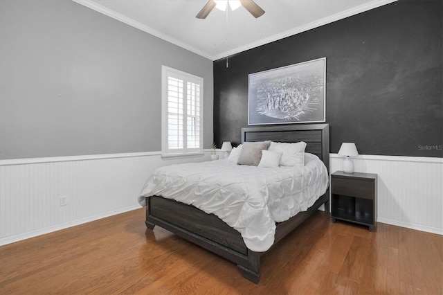 bedroom with crown molding, ceiling fan, wood finished floors, and wainscoting