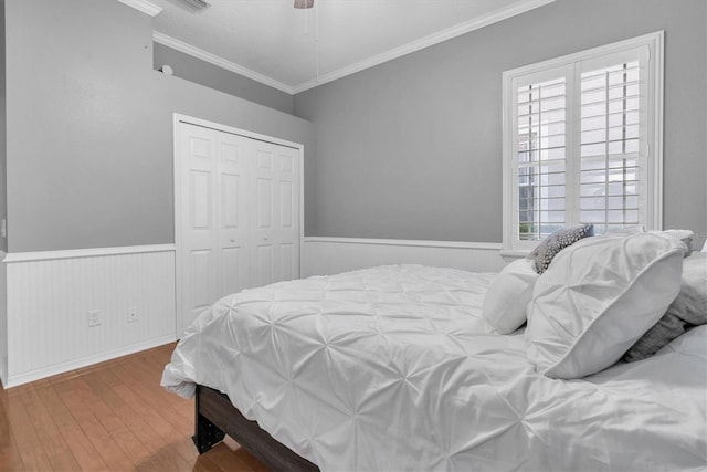 bedroom with a wainscoted wall, a closet, wood finished floors, and crown molding