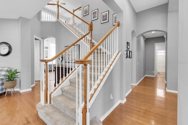 staircase featuring arched walkways, a wealth of natural light, a high ceiling, wood finished floors, and baseboards