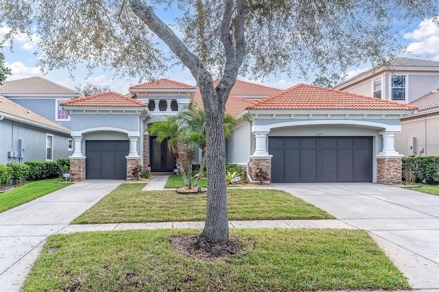 mediterranean / spanish house featuring stucco siding, an attached garage, a front yard, stone siding, and driveway