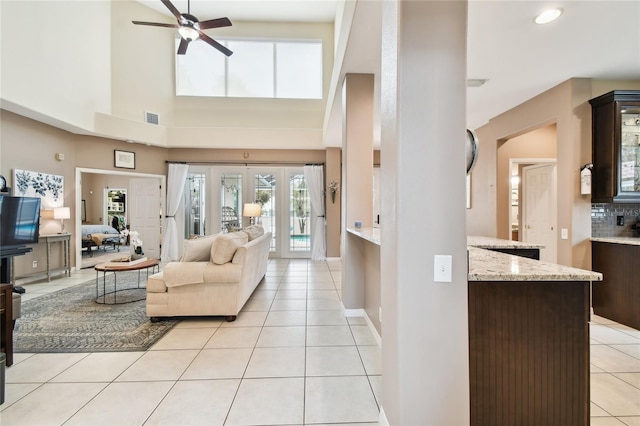 living area with visible vents, a ceiling fan, a high ceiling, light tile patterned flooring, and baseboards