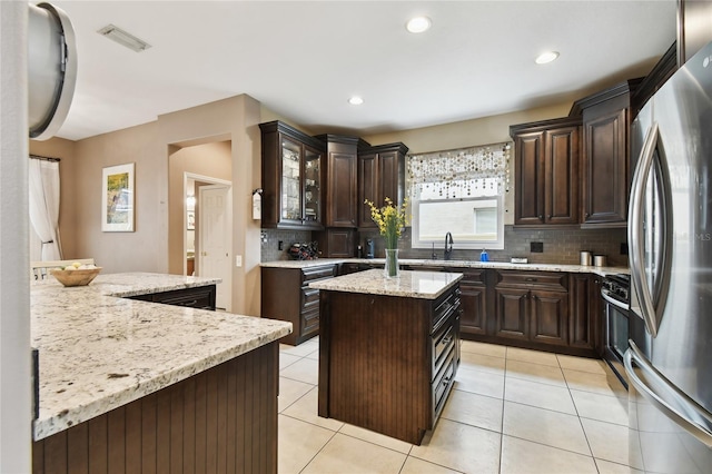 kitchen featuring dark brown cabinetry, light tile patterned floors, appliances with stainless steel finishes, and a kitchen island