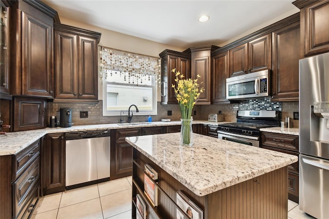 kitchen with a sink, stainless steel appliances, light stone counters, and light tile patterned floors