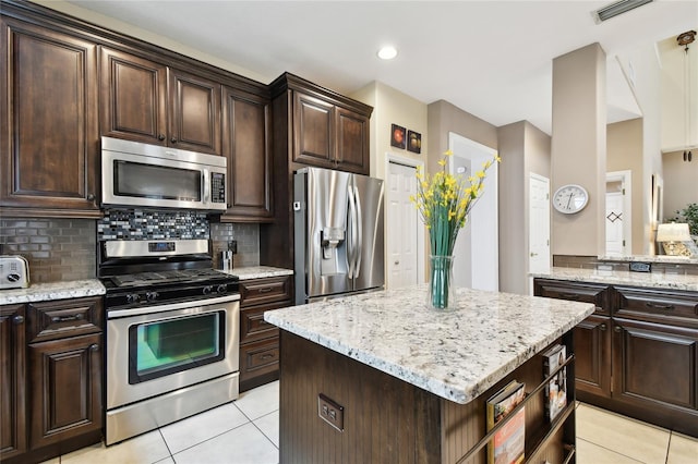 kitchen with backsplash, stainless steel appliances, light tile patterned floors, light stone countertops, and dark brown cabinets