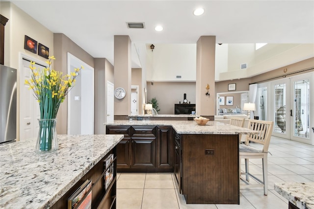 kitchen featuring visible vents, light stone counters, french doors, a kitchen breakfast bar, and freestanding refrigerator