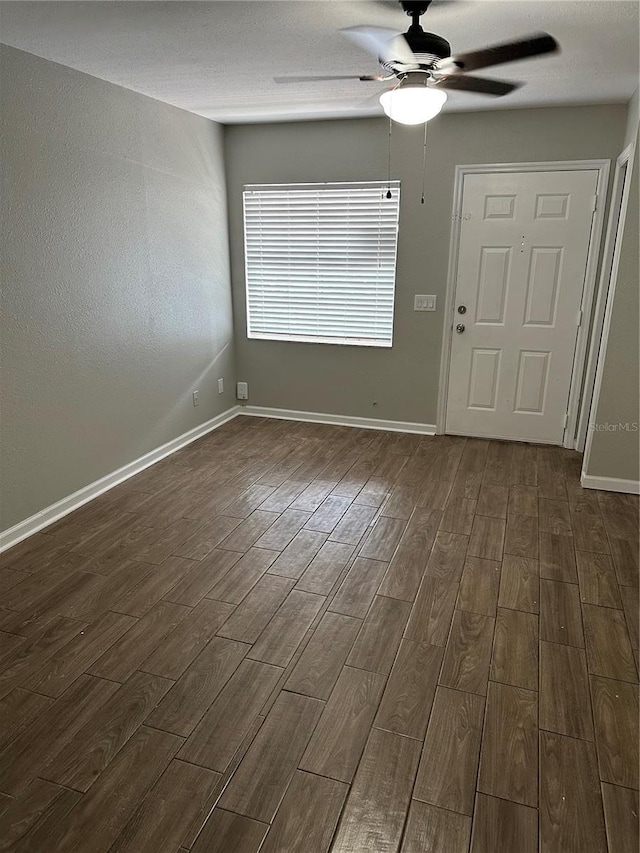 spare room with a ceiling fan, baseboards, and dark wood-type flooring