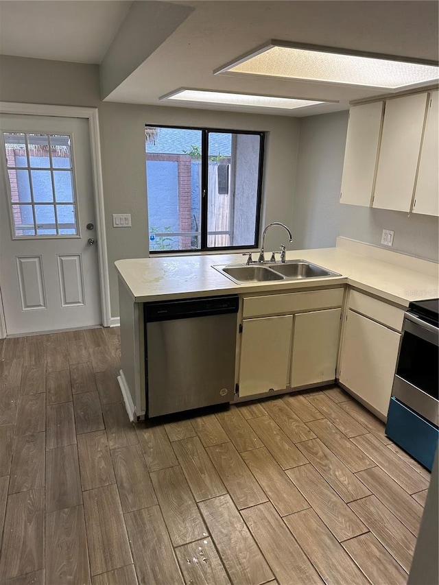 kitchen with light countertops, appliances with stainless steel finishes, a sink, light wood-type flooring, and a peninsula