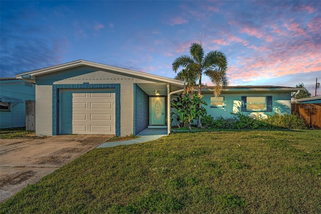 ranch-style house featuring a garage, concrete block siding, a front lawn, and concrete driveway