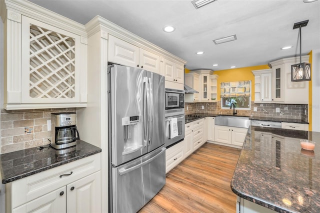 kitchen featuring a sink, hanging light fixtures, appliances with stainless steel finishes, light wood finished floors, and glass insert cabinets