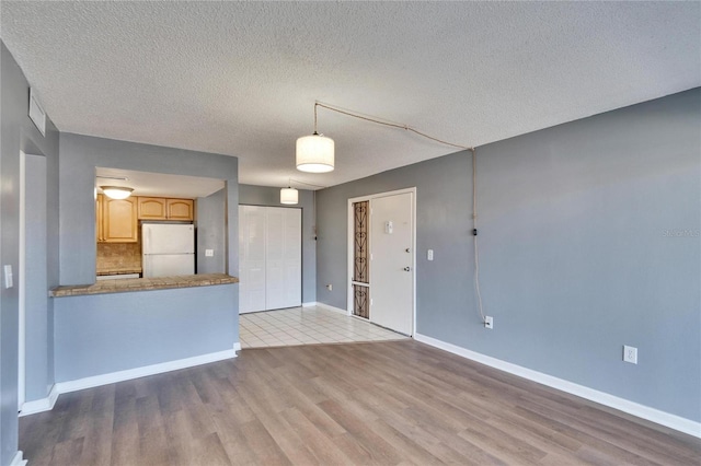 unfurnished living room featuring a textured ceiling, baseboards, and wood finished floors