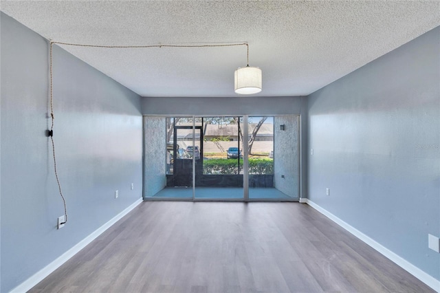 empty room with a textured ceiling, baseboards, and wood finished floors