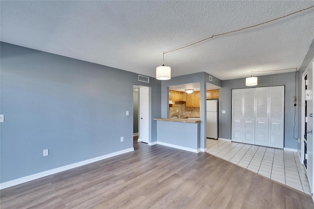 unfurnished living room with a textured ceiling, light wood-type flooring, visible vents, and baseboards