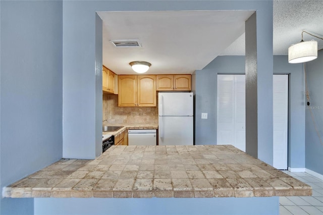 kitchen featuring light brown cabinets, white appliances, visible vents, tile counters, and decorative backsplash