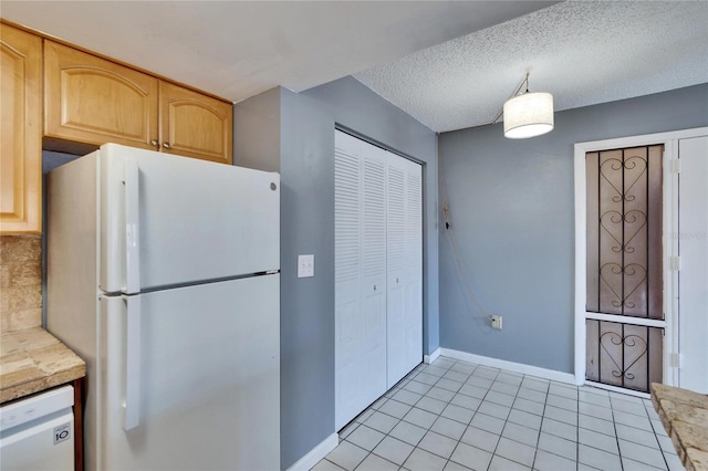 kitchen with light tile patterned floors, a textured ceiling, light brown cabinets, white appliances, and baseboards