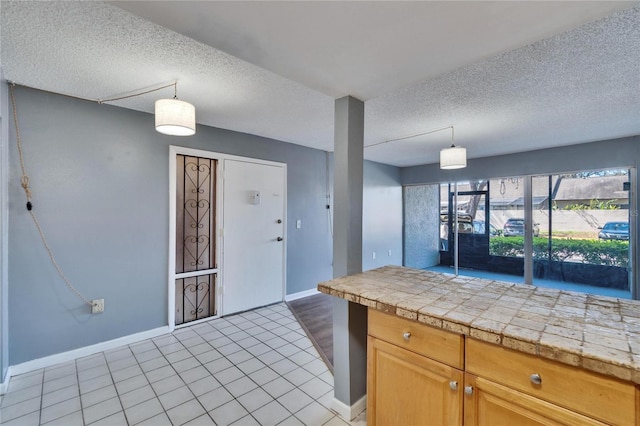 kitchen featuring decorative light fixtures, tile countertops, light tile patterned floors, a textured ceiling, and baseboards