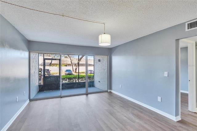 empty room featuring a textured ceiling, wood finished floors, visible vents, and baseboards