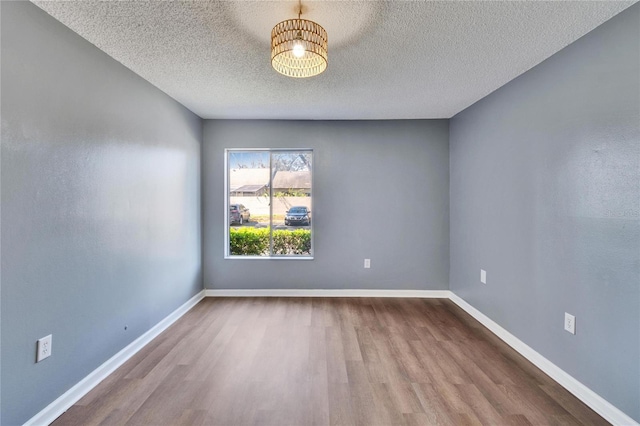 empty room featuring a textured ceiling, baseboards, and wood finished floors