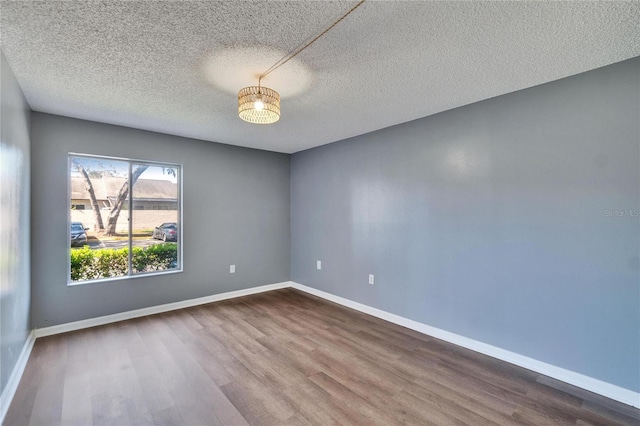 unfurnished room featuring a textured ceiling, dark wood finished floors, and baseboards