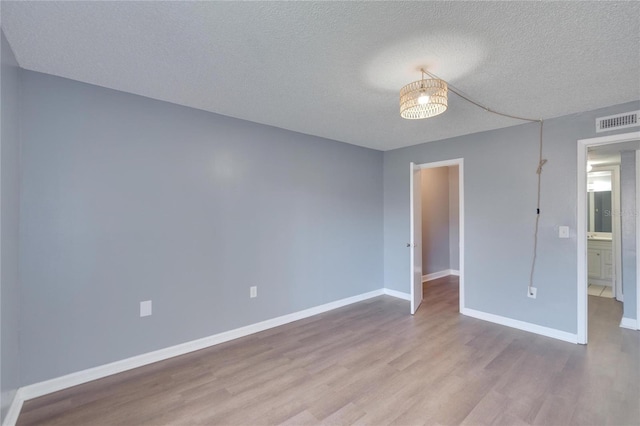 empty room with baseboards, a textured ceiling, visible vents, and wood finished floors