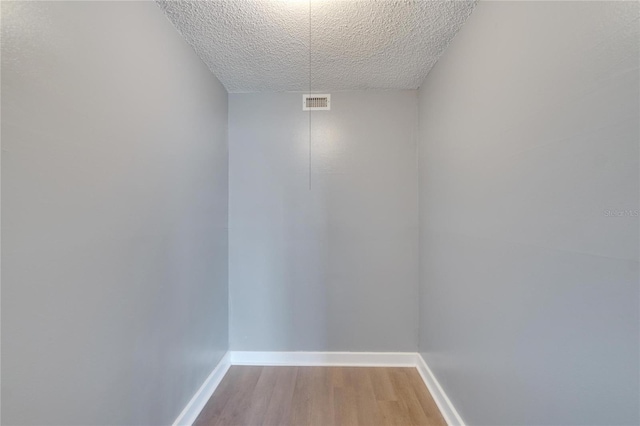 interior space with baseboards, a textured ceiling, visible vents, and wood finished floors