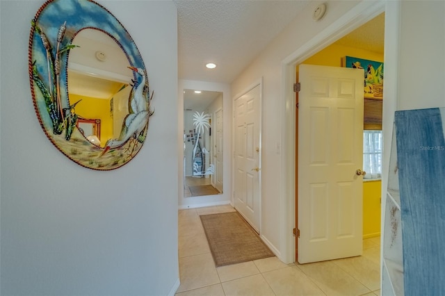 hall with light tile patterned floors, a textured ceiling, and baseboards