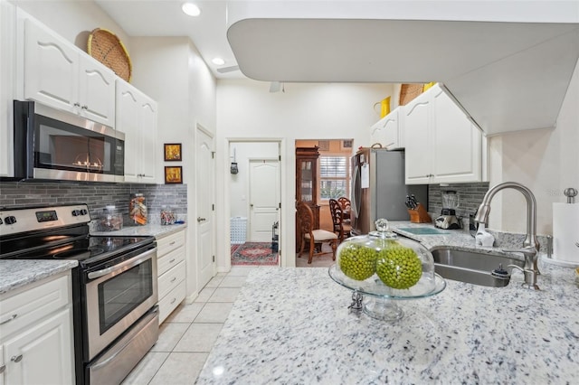 kitchen featuring white cabinets, light stone countertops, stainless steel appliances, a sink, and light tile patterned flooring