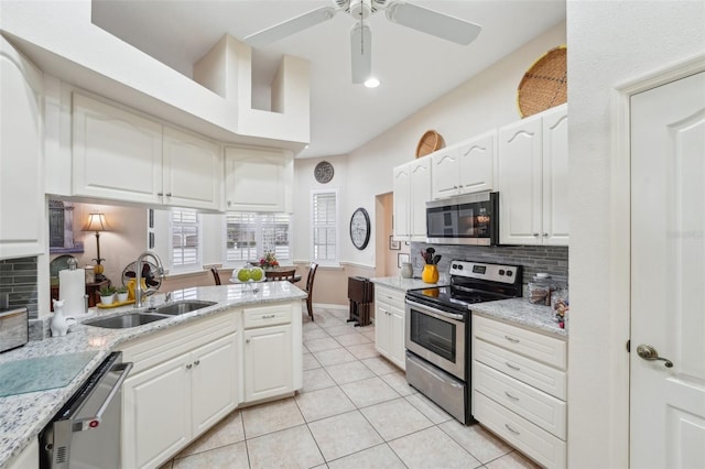 kitchen featuring stainless steel appliances, white cabinets, a sink, and light stone countertops