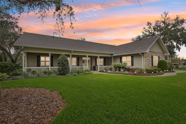 ranch-style home with stone siding, a front lawn, covered porch, and roof with shingles