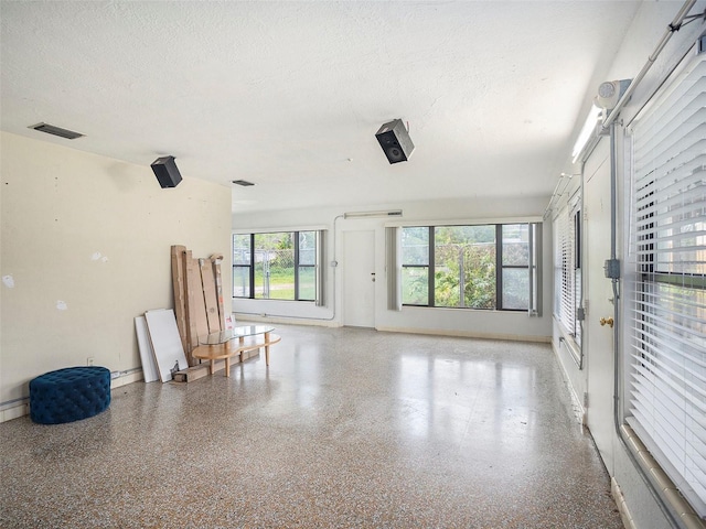 interior space featuring visible vents, a textured ceiling, baseboards, and speckled floor