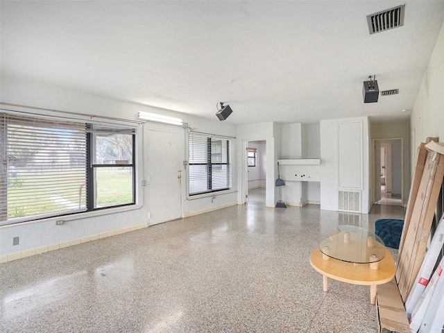 unfurnished living room with speckled floor, visible vents, and baseboards