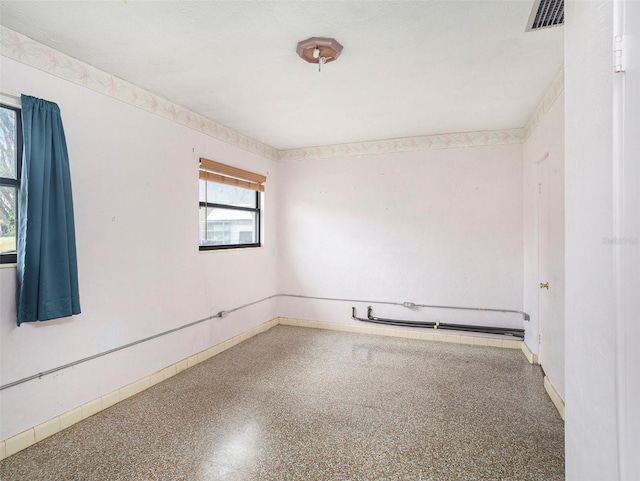 unfurnished room with baseboards, visible vents, and speckled floor