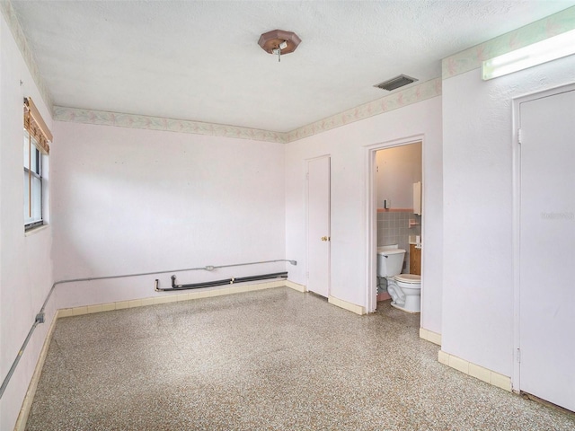 spare room with a textured ceiling, speckled floor, visible vents, baseboards, and tile walls