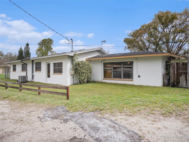 ranch-style house featuring central AC unit, fence, a front lawn, and stucco siding