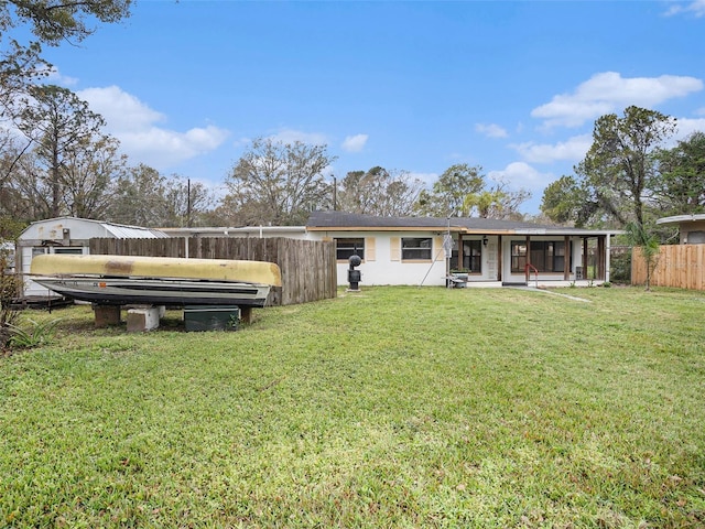 rear view of house with a sunroom, fence, and a yard