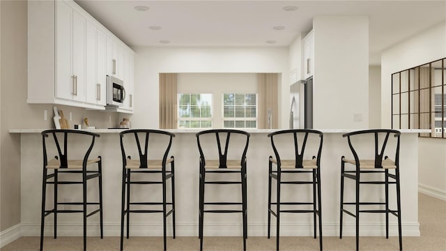 kitchen featuring appliances with stainless steel finishes, light countertops, a kitchen breakfast bar, and white cabinetry