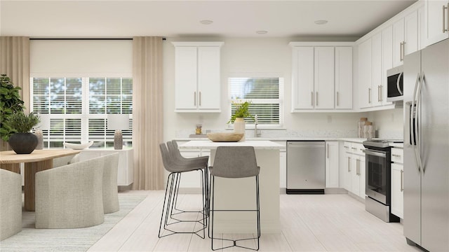 kitchen with stainless steel appliances, a breakfast bar, a kitchen island, white cabinets, and light countertops