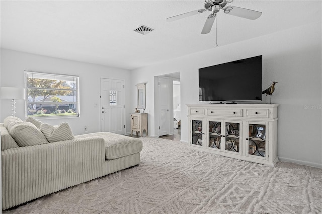 living room featuring ceiling fan, visible vents, baseboards, and light colored carpet