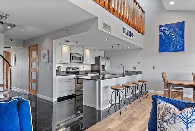 kitchen with stainless steel appliances, a peninsula, white cabinets, dark countertops, and a kitchen bar