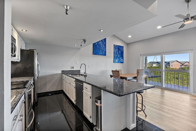 kitchen with stainless steel appliances, white cabinetry, a sink, dark stone counters, and a kitchen breakfast bar