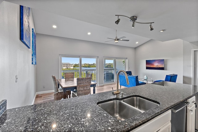 kitchen with dark stone countertops, wood finished floors, vaulted ceiling, white cabinetry, and a sink