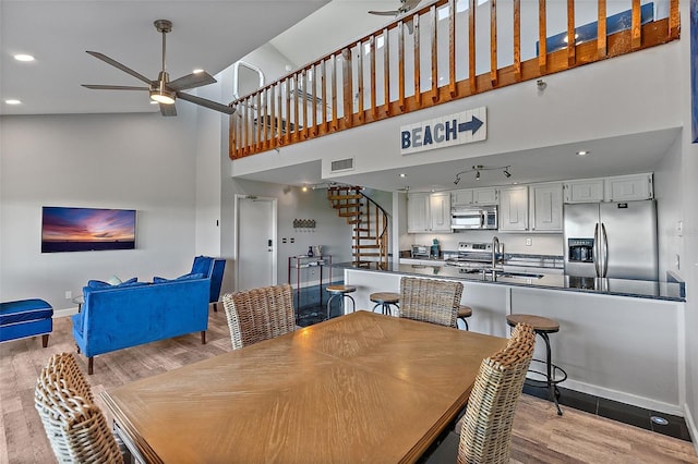 dining space with light wood-type flooring, visible vents, ceiling fan, and stairs