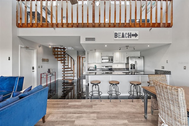 kitchen featuring visible vents, white cabinets, appliances with stainless steel finishes, a breakfast bar area, and a high ceiling